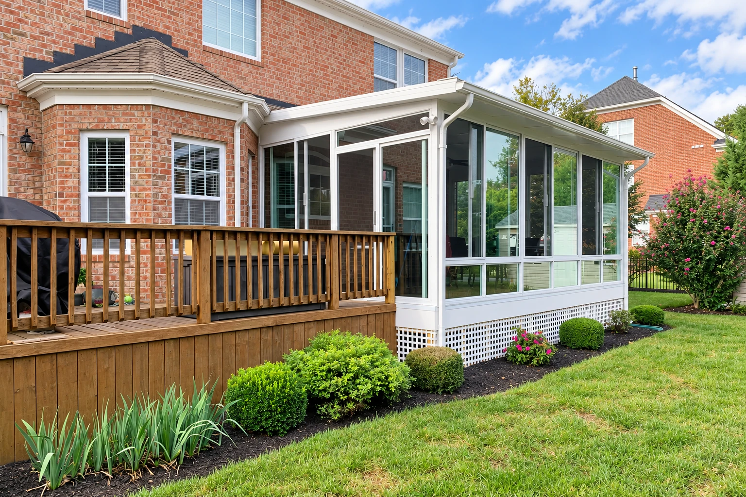 Brick home with a deck-to-sunroom conversion, featuring a white-framed glass enclosure beside a wooden deck.