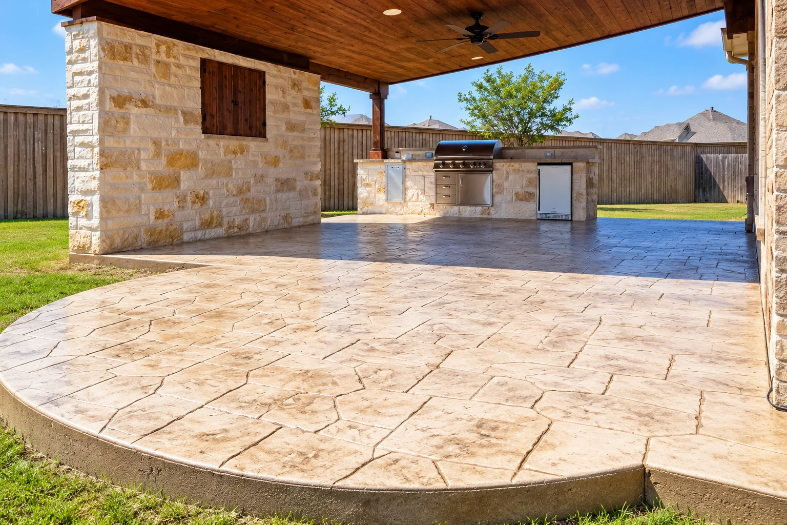 Covered patio with a wood-paneled ceiling, stone outdoor kitchen, and broad stamped-concrete floor.