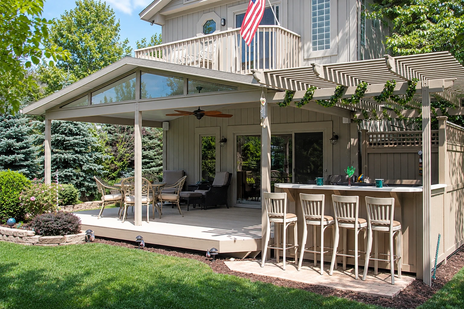 Covered patio with a broad gabled roof, outdoor seating, bar stools and an overhead pergola attached to a house.