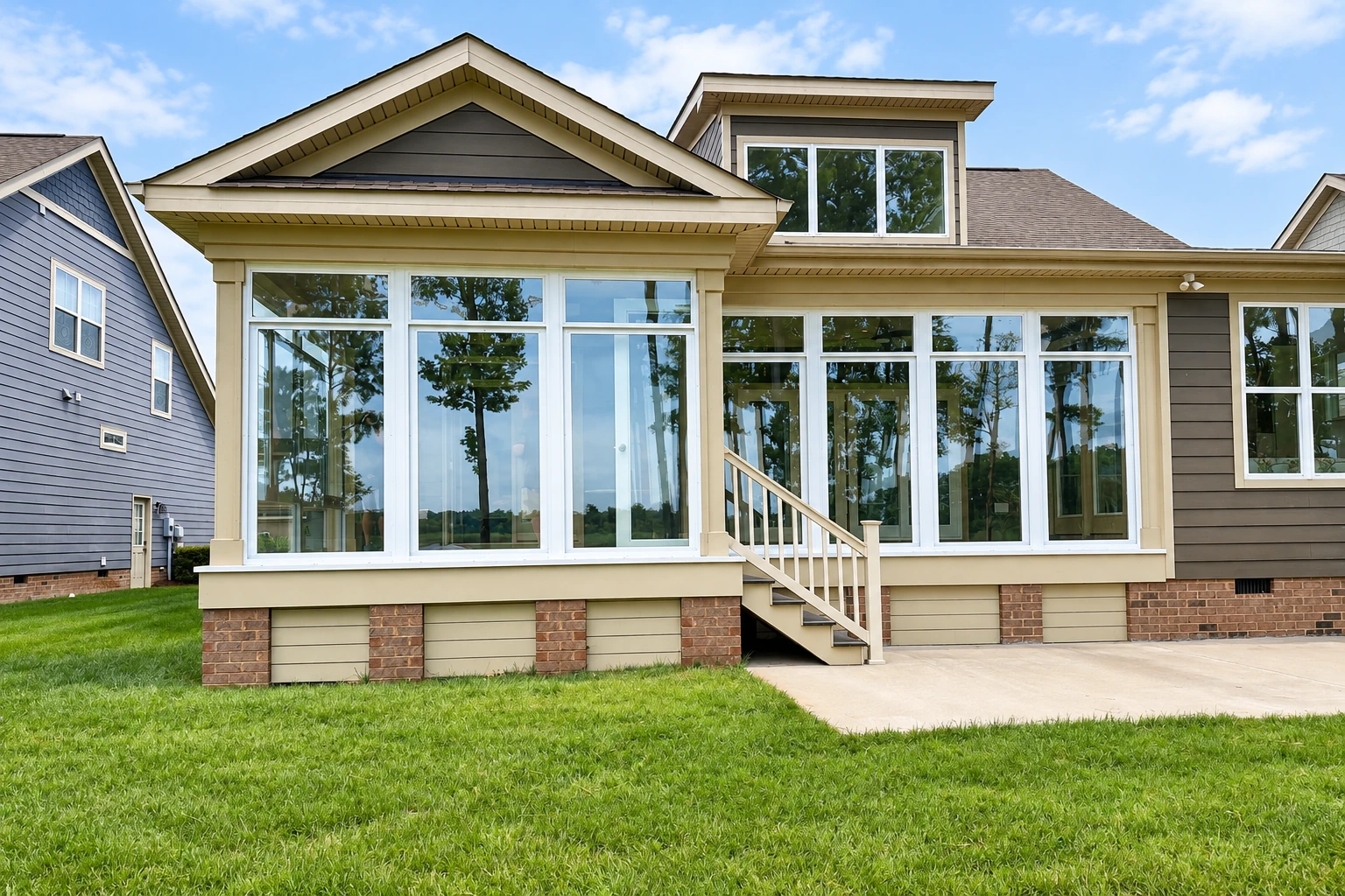 A beige house features a wide sunroom with white-framed windows and exterior steps opening onto a lawn.