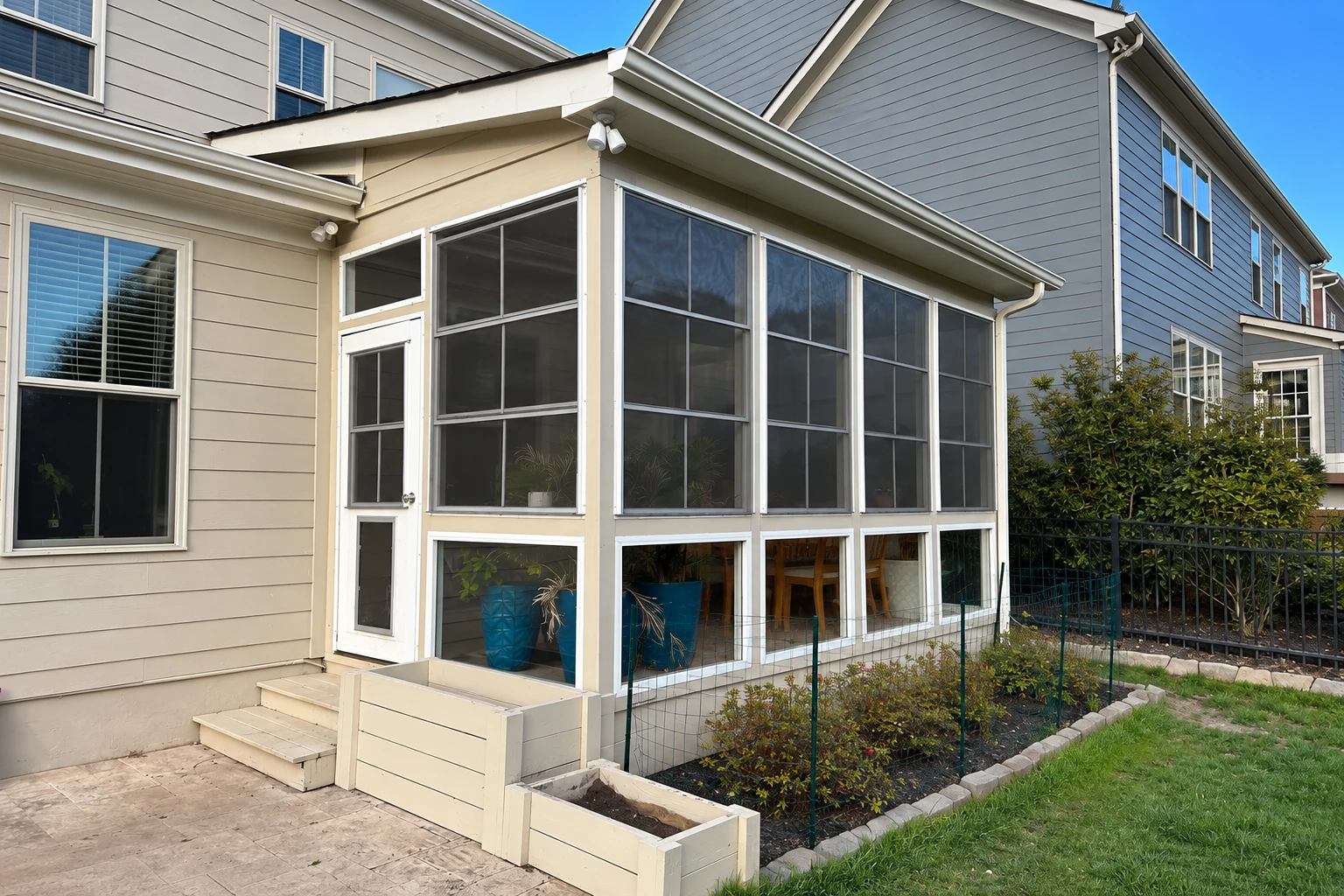 Three-season sunroom with screened walls attached to a house, beside a small fenced garden and patio steps.