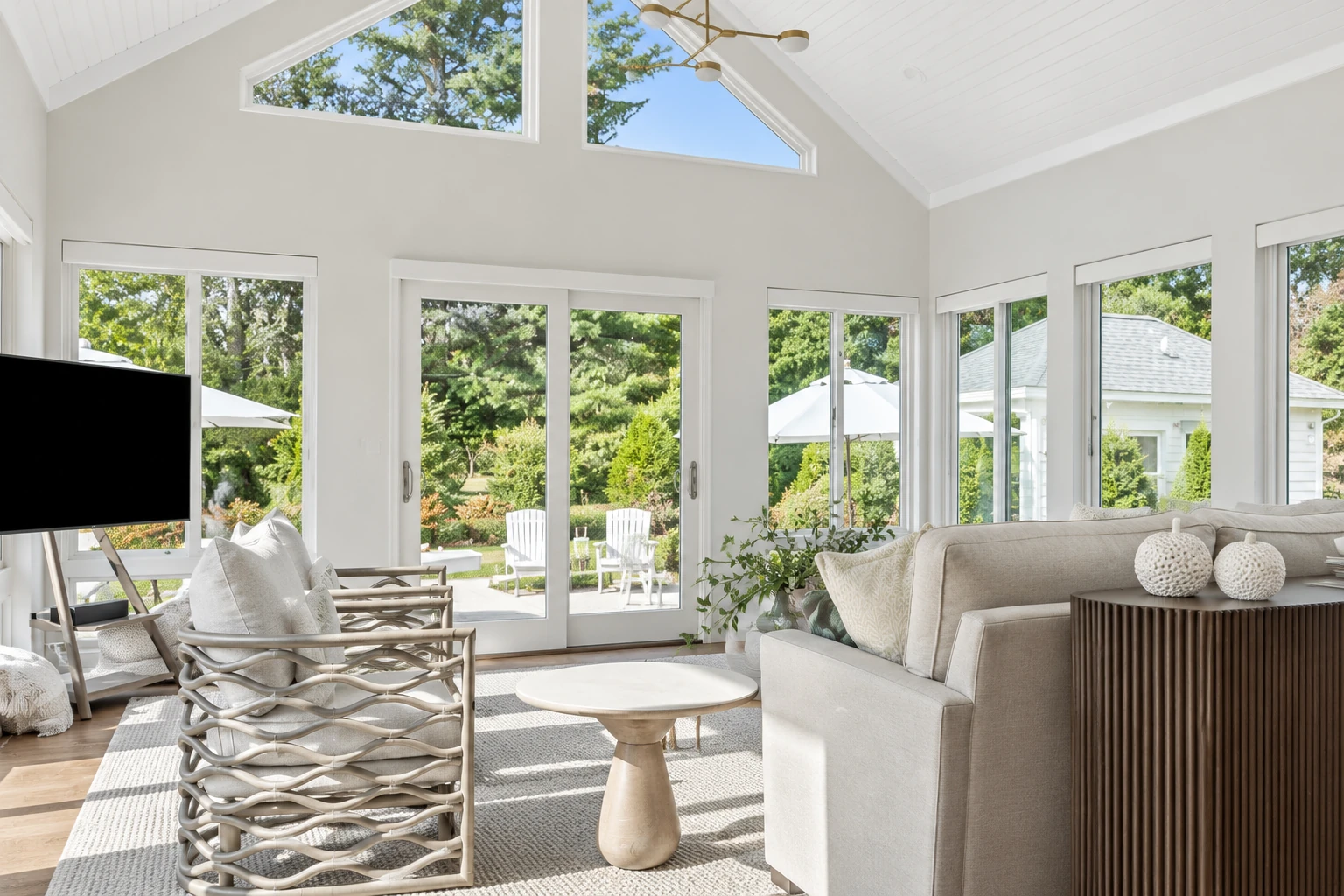 Bright vinyl sunroom with white framing, vaulted ceiling, large windows, neutral seating, and views of a garden patio.